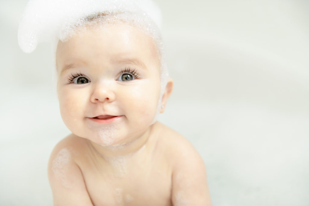 A Baby girl bathes in a bath with foam and soap bubbles